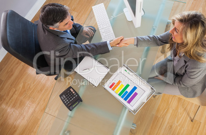 Two business people having a handshake above a desk