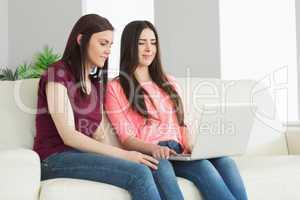 Two teenagers sitting on a sofa and watching a laptop