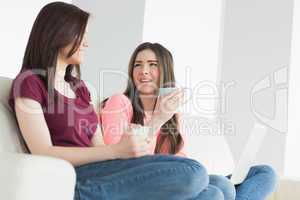 Two laughing girls sitting on a sofa enjoying a beverage and hol