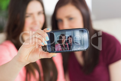 Two smiling girls sitting on a sofa taking a photo of themselves