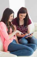 Two smiling girls sitting on a sofa using a tablet pc