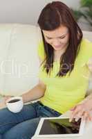 Smiling girl sitting on a sofa using a tablet pc and holding a c