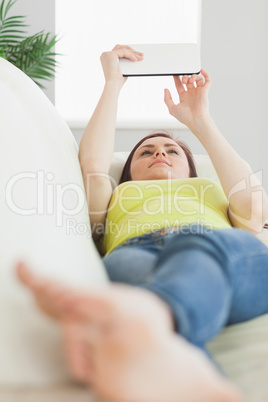 Happy teen lying on a sofa using a tablet pc