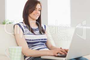 Smiling girl using her laptop sitting on a sofa
