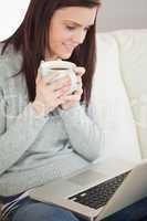 Relaxed girl sitting on a sofa holding a cup of coffee and looki