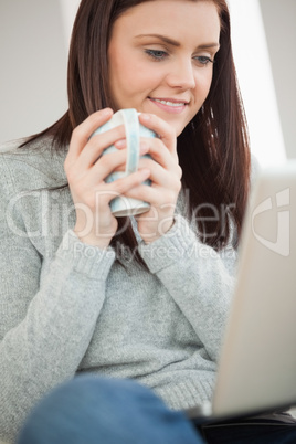 Smiling girl sitting on a sofa holding a cup of coffee and looki