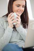 Smiling girl sitting on a sofa holding a cup of coffee and looki
