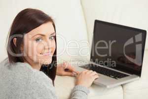 Smiling girl using a laptop on a sofa looking at camera