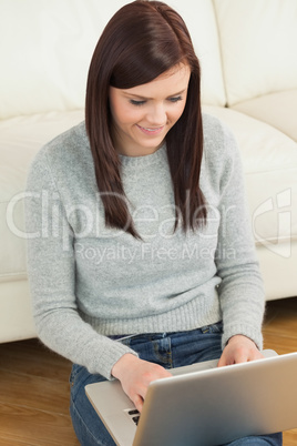 Smiling girl using a laptop sitting against a sofa