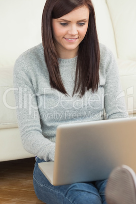 Happy girl using a laptop sitting against a sofa