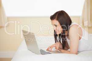 Cheerful girl using a laptop lying on her bed