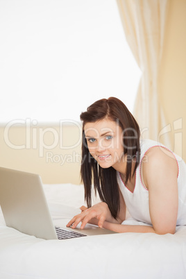 Content girl using a laptop lying on her bed