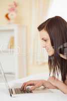 Pretty young girl using a laptop lying on her bed