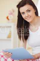 Happy girl sitting on bed using tablet looking at camera