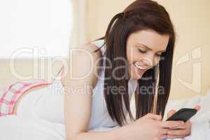 Smiling girl using a mobile phone lying on a bed