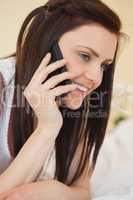 Smiling girl calling someone with a mobile phone lying on a bed