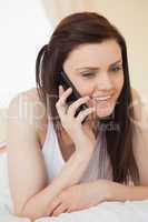 Happy girl calling someone with a mobile phone lying on a bed