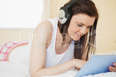 Smiling girl listening to music and using a tablet pc lying on a