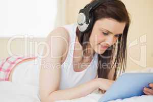 Smiling girl listening to music and using a tablet pc lying on a