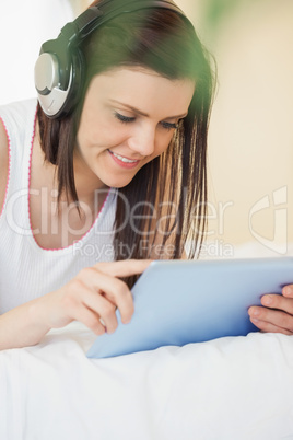 Happy girl listening to music and using a tablet pc lying on a b