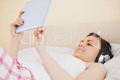 Smiling girl listening music and using a tablet pc lying on a be