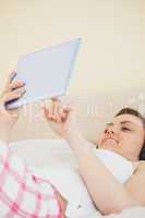 Smiling girl holding a tablet pc lying on a bed