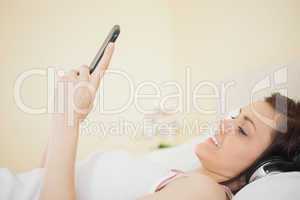 Smiling girl listening music on her smartphone lying on bed