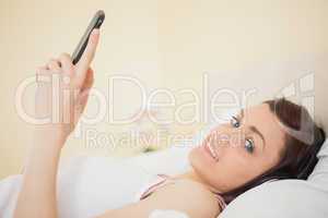 Happy girl listening music on her smartphone lying on bed