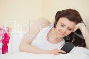 Content girl using a mobile phone lying on a bed