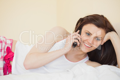 Smiling girl calling someone with a mobile phone lying on a bed