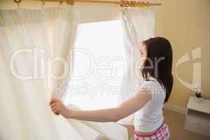 Girl opening curtains in a bedroom