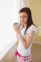 Smiling girl looking at camera and drinking a cup of coffee in a