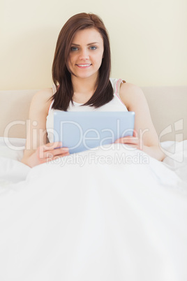 Smiling girl looking at camera using a tablet pc lying on a bed