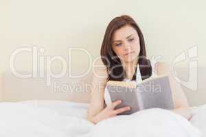 Concentrated girl reading a book lying on a bed