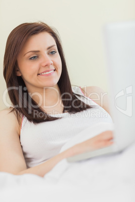Cheerful girl looking and using a laptop lying on a bed