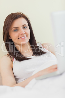 Content girl looking at camera and using a laptop lying on a bed
