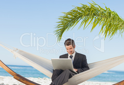Smiling businessman using laptop and sitting in hammock