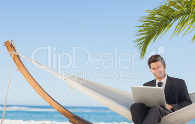 Businessman sitting in hammock using laptop looking at camera