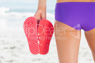 Rear view of a young woman holding flip flops