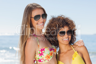 Two friends wearing sunglasses on the beach and smiling