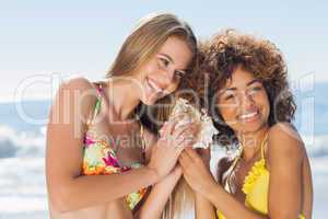 Two girls in bikinis listening to conch shell