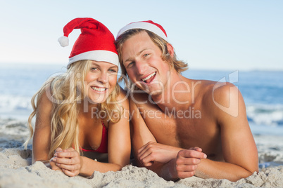 Couple lying on beach wearing christmas hats