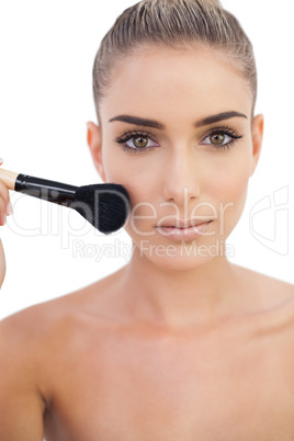 Serious woman applying powder on her cheeks