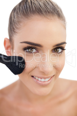 Cheerful woman applying powder on her cheeks
