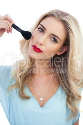 Thoughtful blonde model in blue dress applying make up