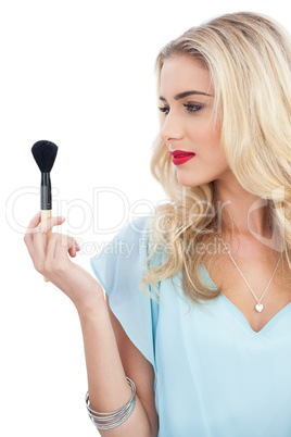 Blonde model in blue dress looking at her blush brush