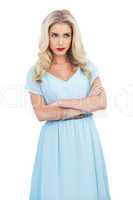 Thoughtful blonde model in blue dress posing crossed arms