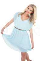 Delighted blonde model in blue dress posing holding her dress