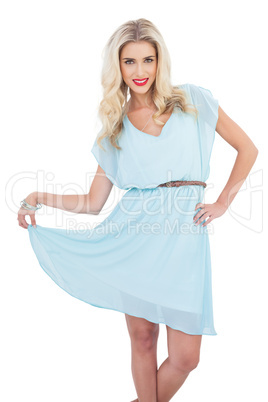 Joyful blonde model in blue dress posing holding her dress Joyful blonde model in blue dress posing holding her dress