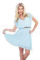 Joyful blonde model in blue dress posing holding her dress